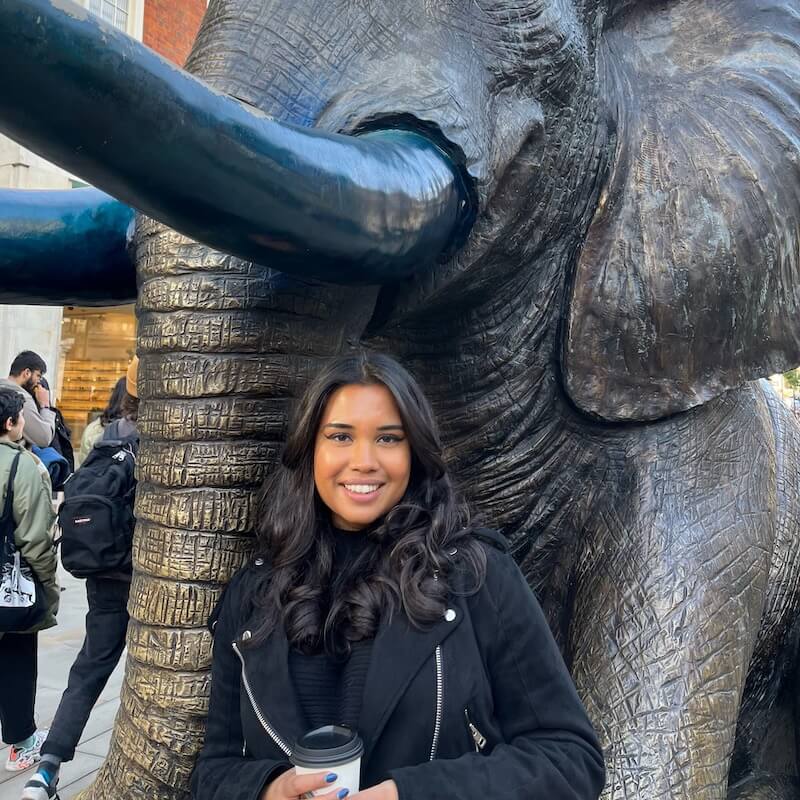 Tangina holding a coffee stood in front of an elephant statue
