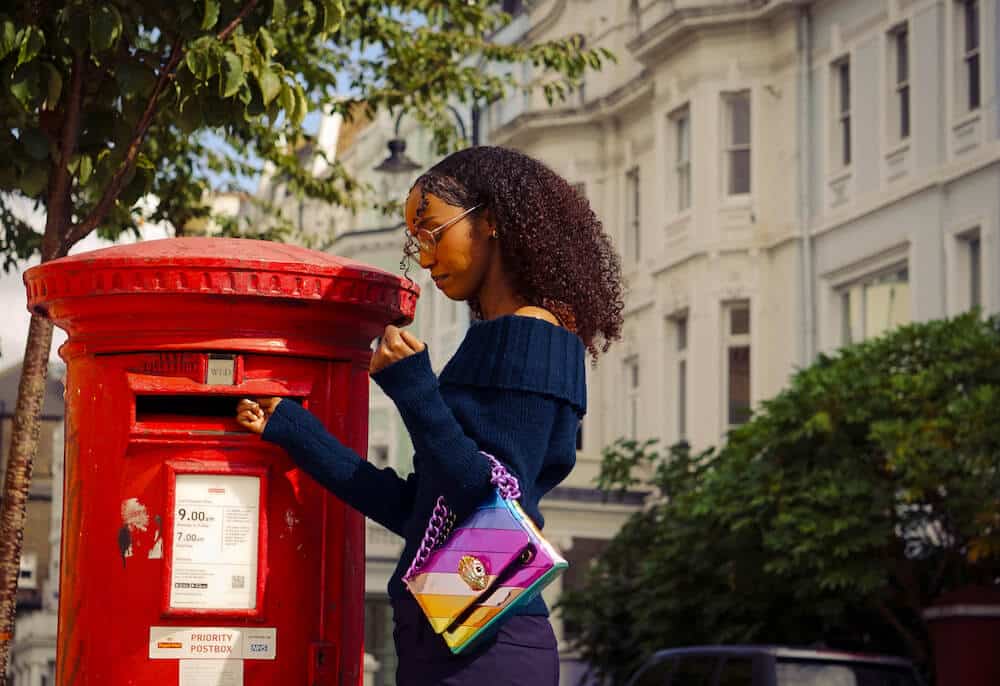 Woman with a Kurt Geiger bag on her shoulder at a red post box